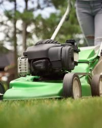female legs of woman using lawn mower.