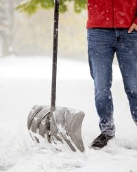 male standing on a snowy field and holding a snow shovel with a blurred background