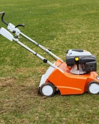 orange grasscutter standing on ground on green grass, special equipment for trimming grass, grass mower oudoor.